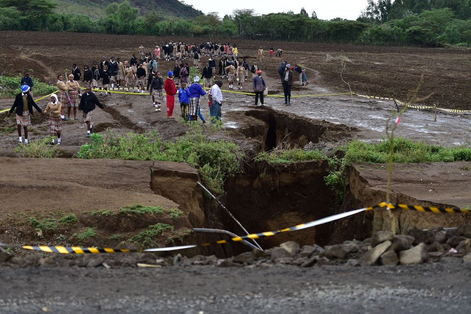 People walking past a large chasm in a road caused by flooding.