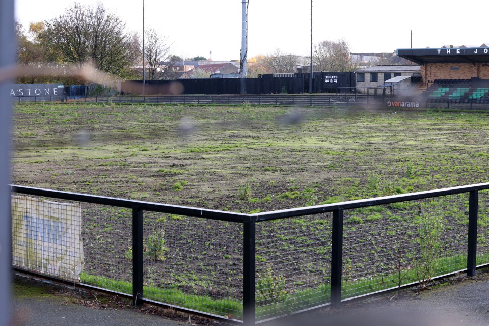 Overgrown, disused football pitch behind a fence.