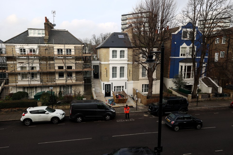 London street scene with houses, one under construction, and parked cars.