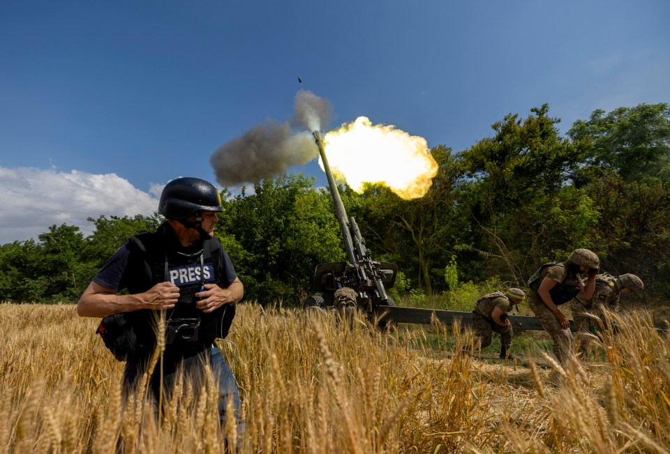 A journalist in body armor watches a Ukrainian artillery unit fire a MSTA-B 152mm artillery gun.