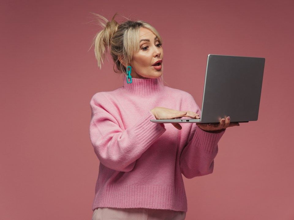 Woman in pink sweater looking surprised at laptop.