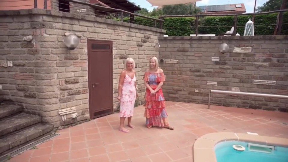 Two women standing by a pool at a house.