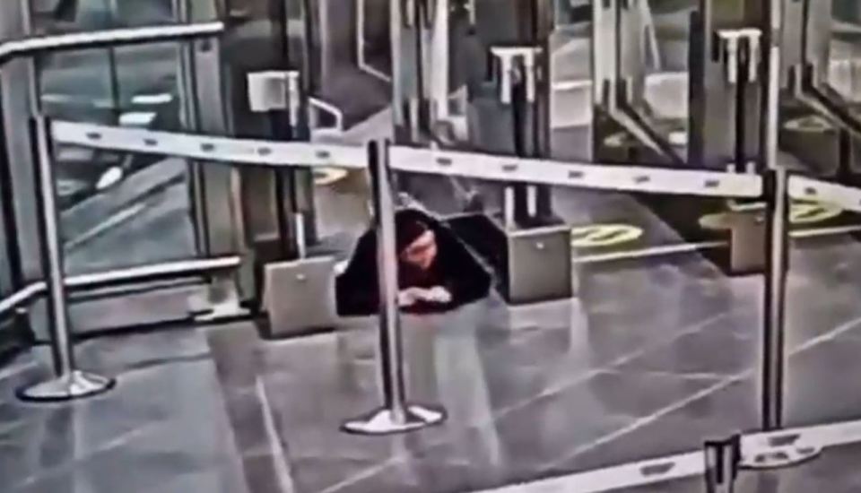 Security footage of a woman crawling under an airport security barrier.