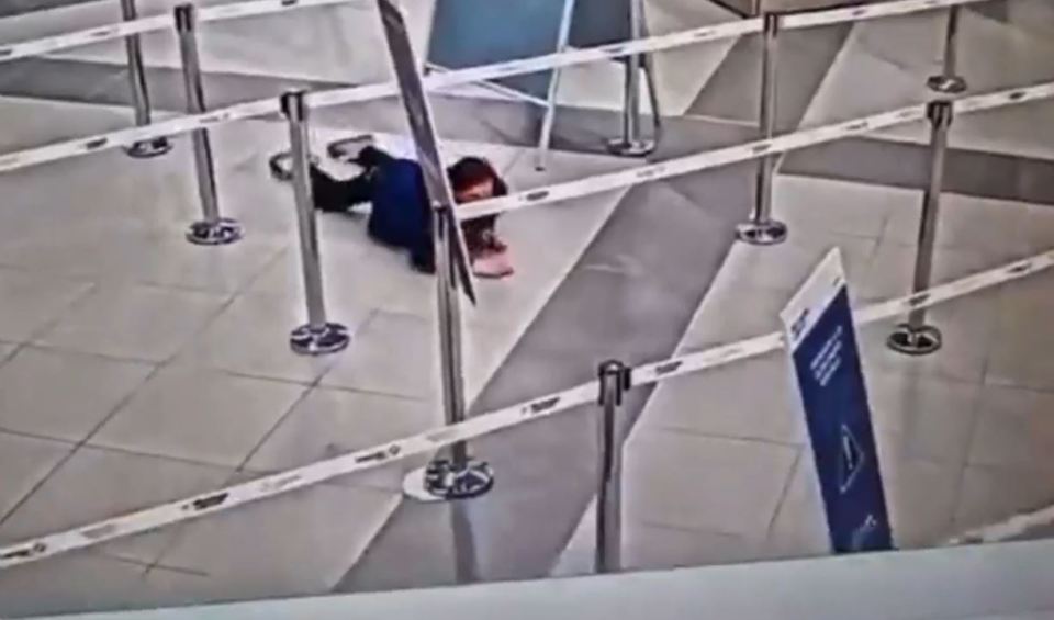 Woman crawling under airport security barrier.