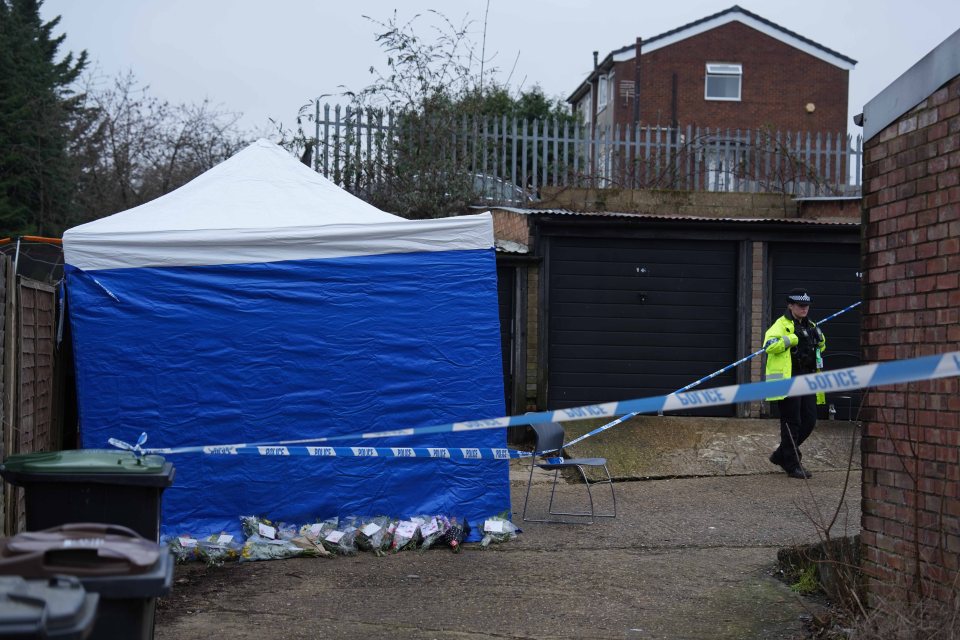 Crime scene with police tape, a blue tent, and flowers.