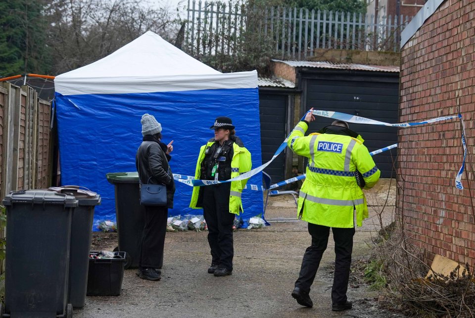 Police officers at a crime scene with police tape and floral tributes.