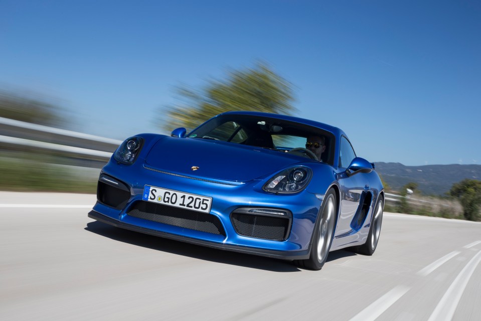 Blue Porsche Cayman GT4 driving on a road.