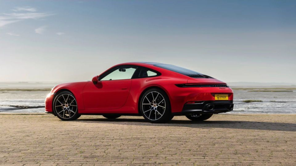 Red Porsche 911 Carrera parked by the sea.