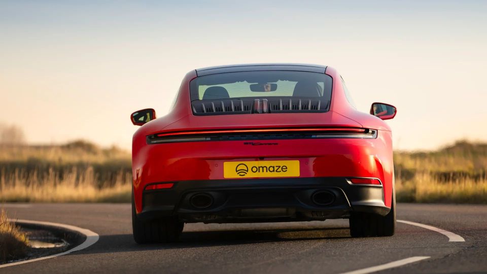 Rear view of a red Porsche 911 Carrera with an Omaze license plate.