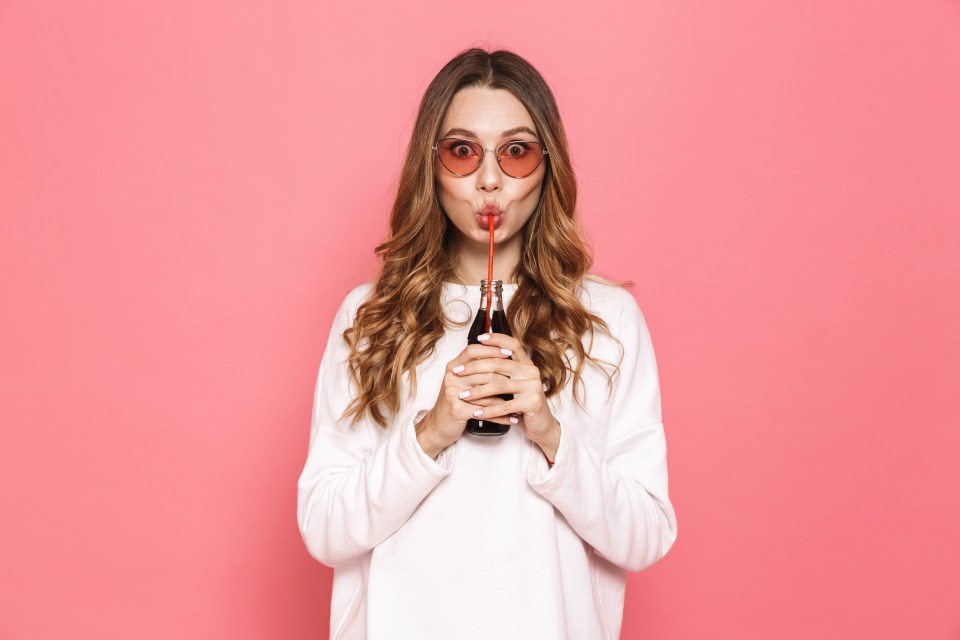 Woman in sunglasses drinking from a bottle with a straw.