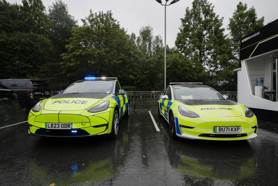 Two Tesla police cars parked in a wet parking lot.