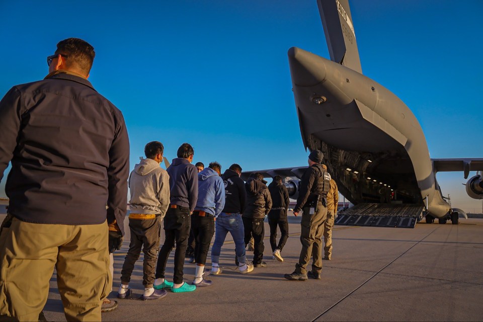 Guatemalan nationals chained together on a tarmac near a military transport plane.