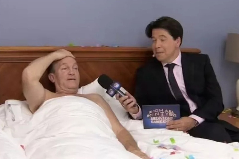 Michael McIntyre interviewing a shirtless Bradley Walsh in bed.