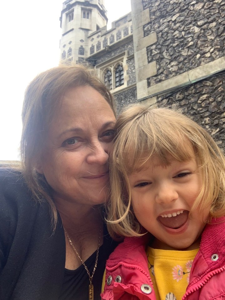 A woman and young girl smile for a selfie in front of a stone building.