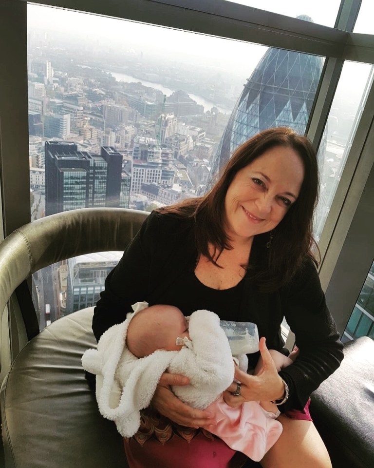 Woman feeding baby in high-rise with city view.