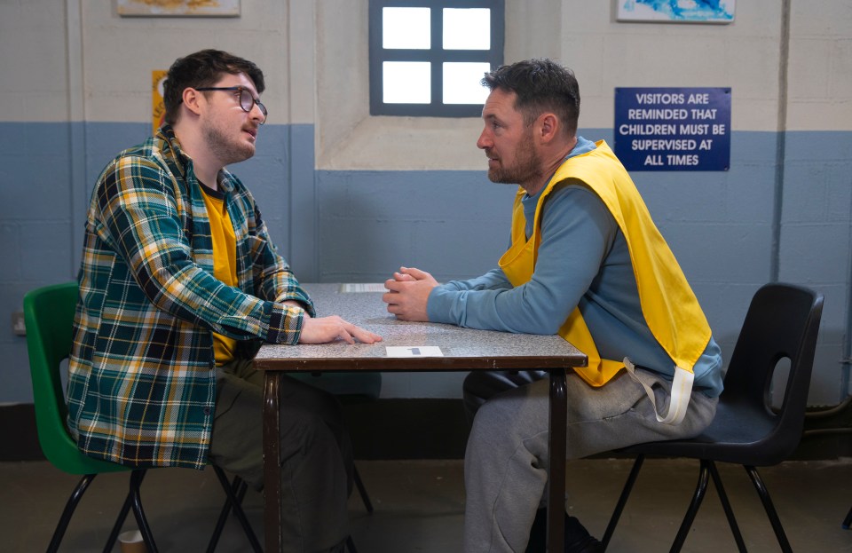 Two men in prison visiting clothes sit across a table from each other.