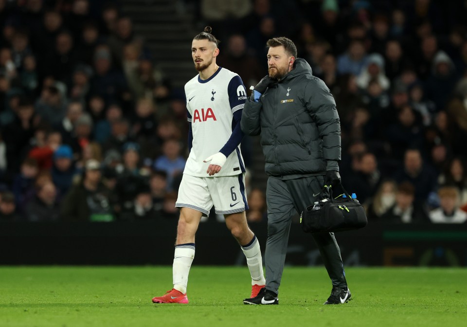 Radu Dragusin of Tottenham Hotspur leaves the pitch with an injury, assisted by a medical professional.