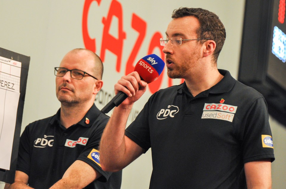 Referee Huw Ware speaking into a microphone at a darts competition.