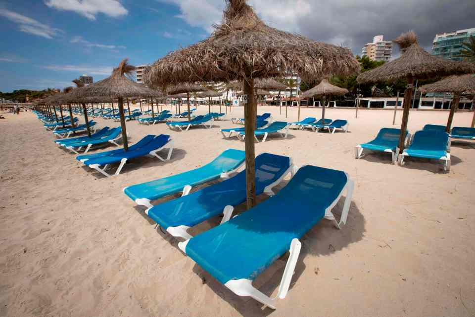 Empty beach chairs and straw umbrellas on a sandy beach.