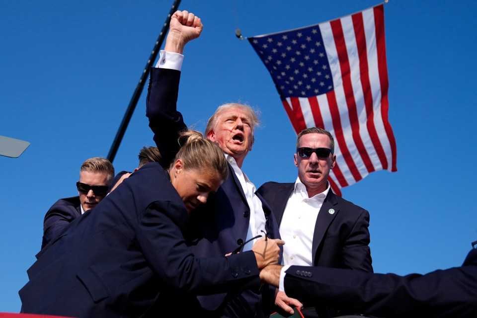 Donald Trump at a rally, appearing injured, surrounded by Secret Service agents.