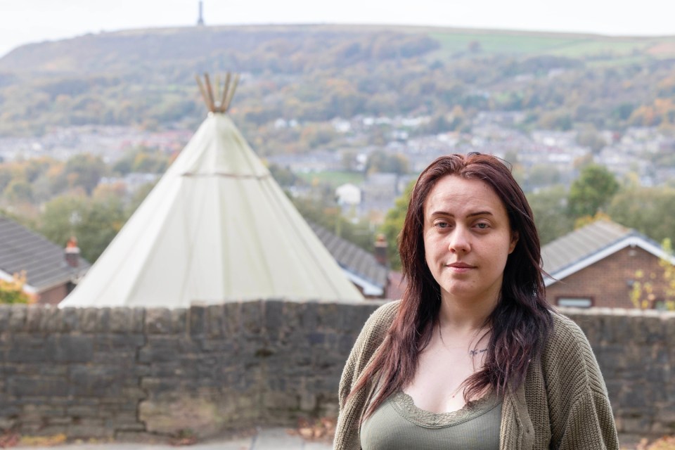 Woman standing in front of teepee, looking at camera.