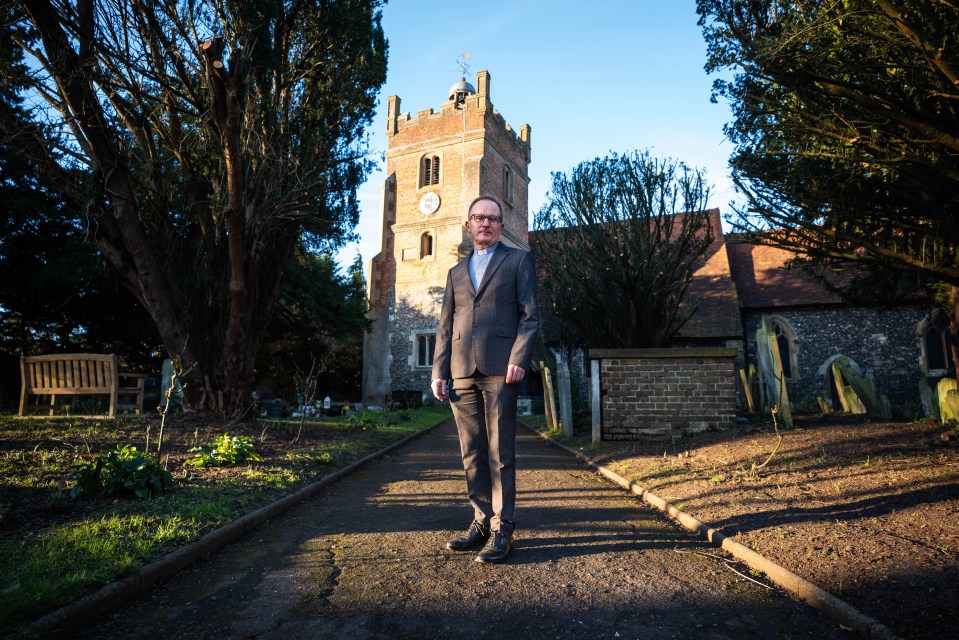 A priest stands outside St Mary the Virgin Church in Harmondsworth, UK.