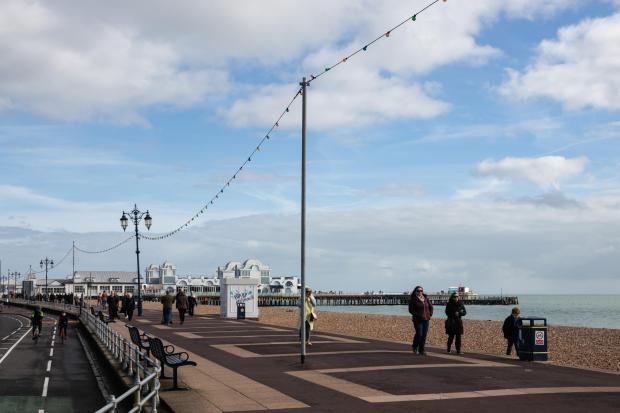 People walking along a beach with a pier in the background.