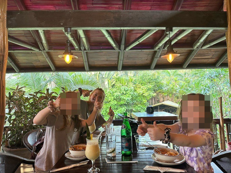 Hannah Spearitt with her children giving thumbs up at an outdoor restaurant.