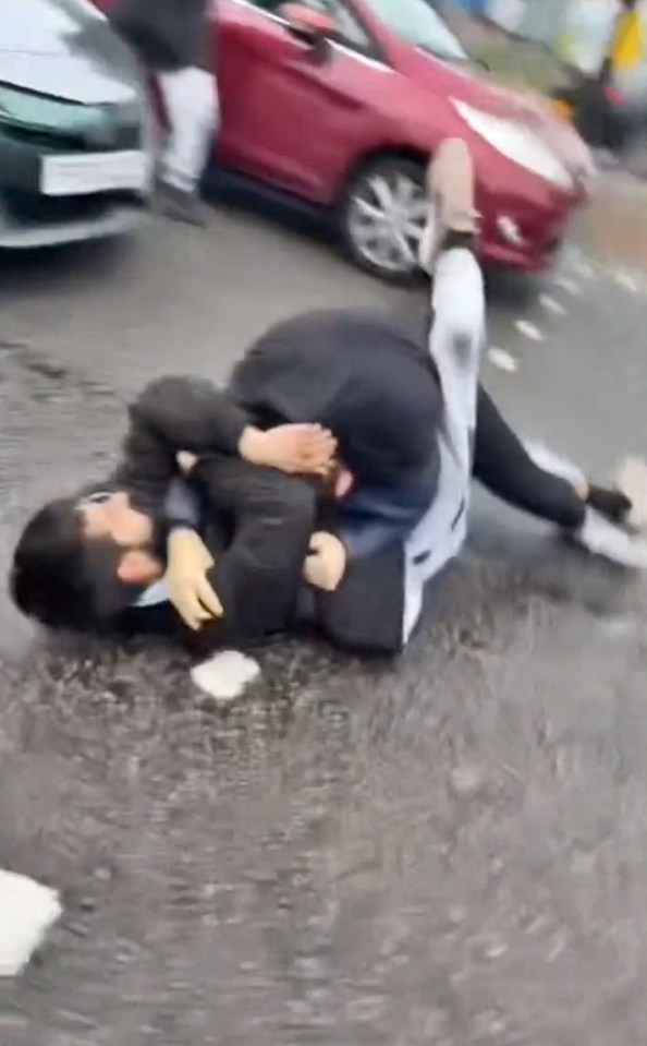 Two men wrestling on a road.