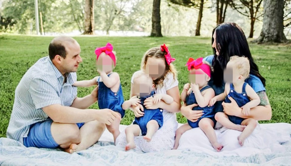 Family photo of parents and five young children sitting on a blanket outdoors.