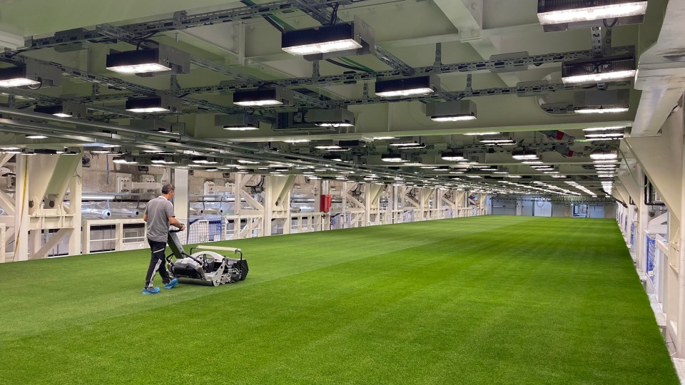 A person uses a machine to maintain a large indoor field of artificial turf at the Santiago Bernabéu Stadium.