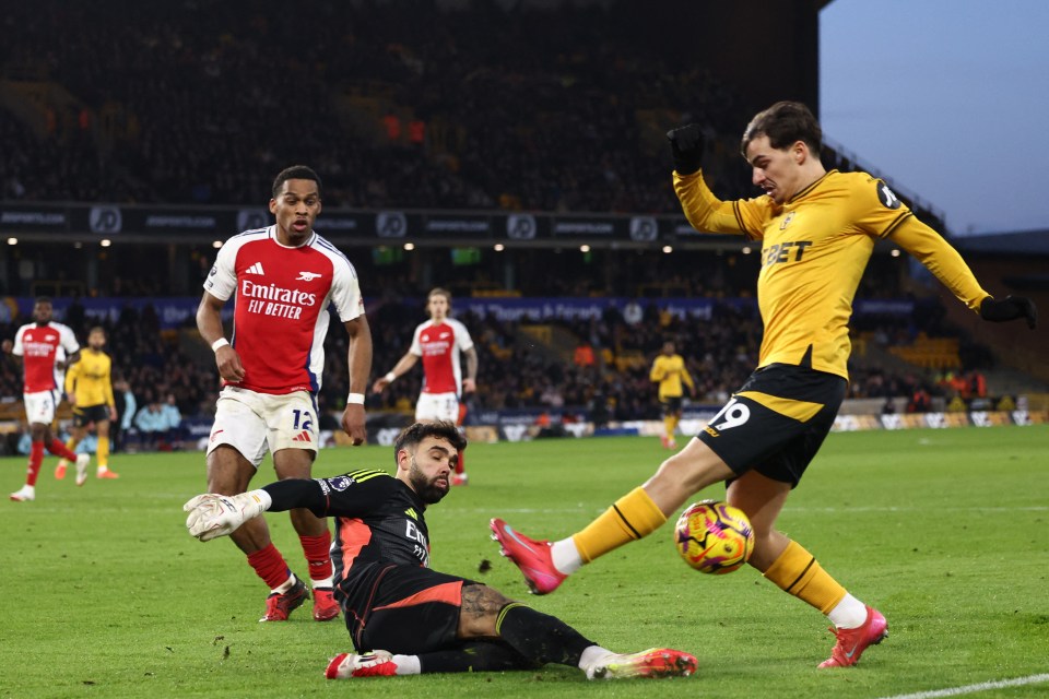 Arsenal's goalkeeper diving to save a shot from a Wolverhampton Wanderers player.