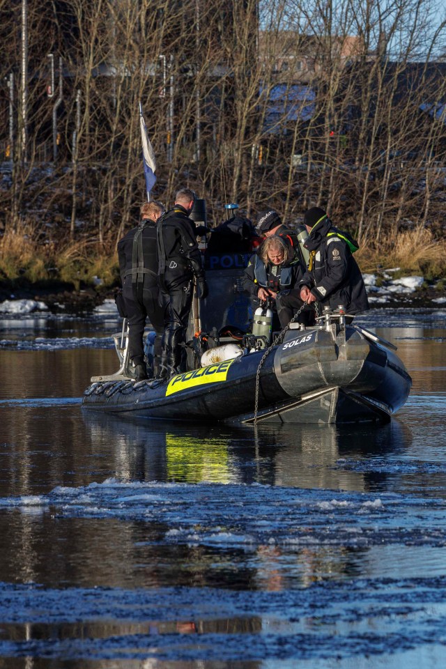 Police divers searching a river from a boat.