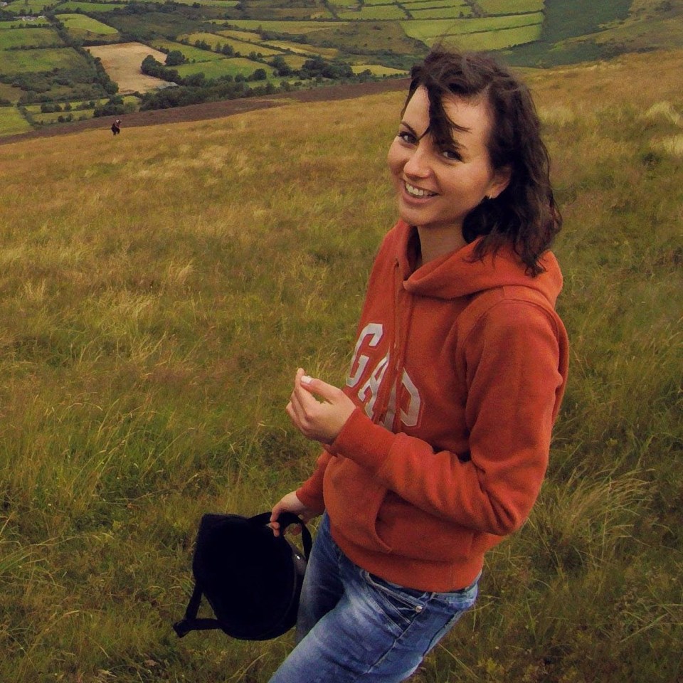 Woman in orange hoodie holding helmet in grassy field.