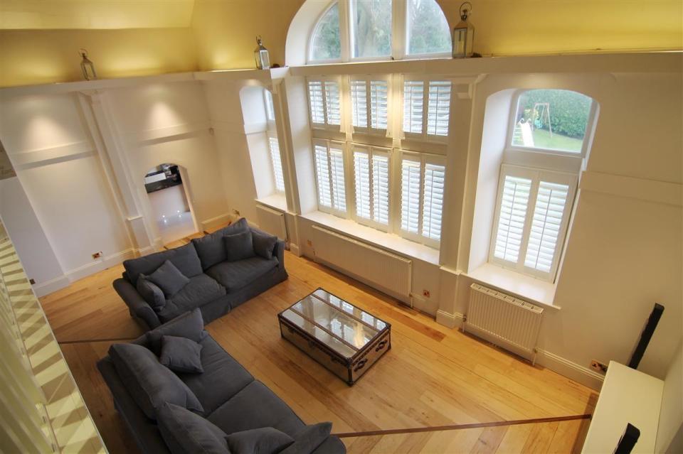 Living room with hardwood floors, two gray sofas, a coffee table, and large windows with white shutters.