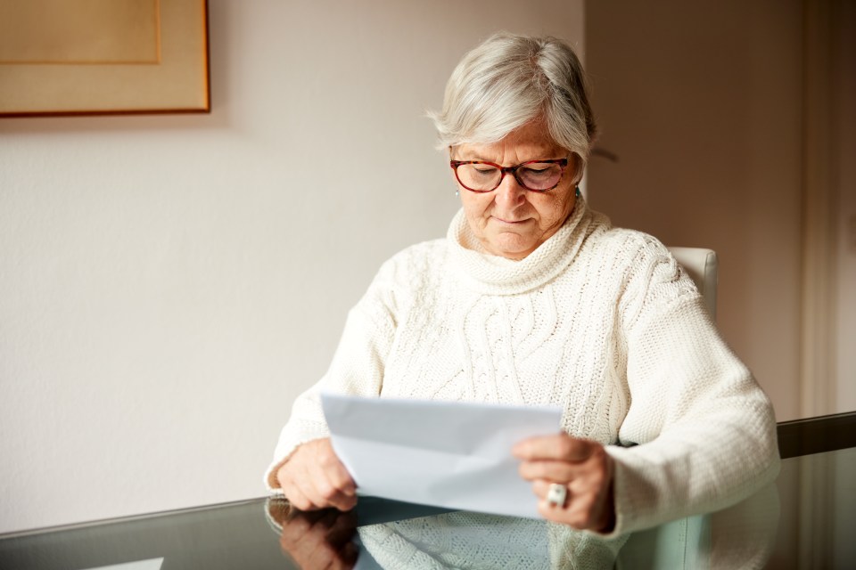 Senior woman reading mail at a table.