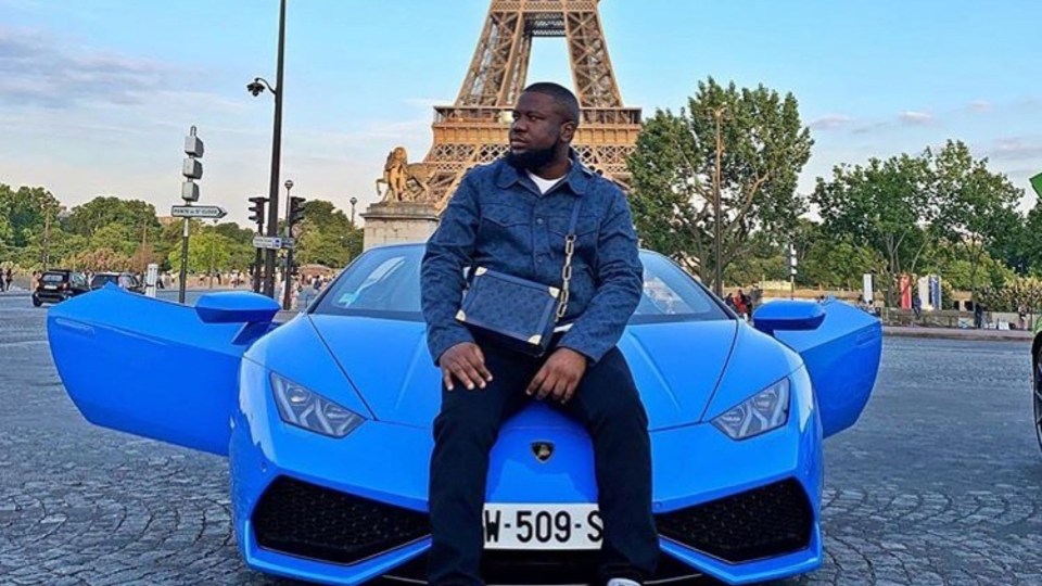 Man sitting on a blue Lamborghini in Paris with the Eiffel Tower in the background.