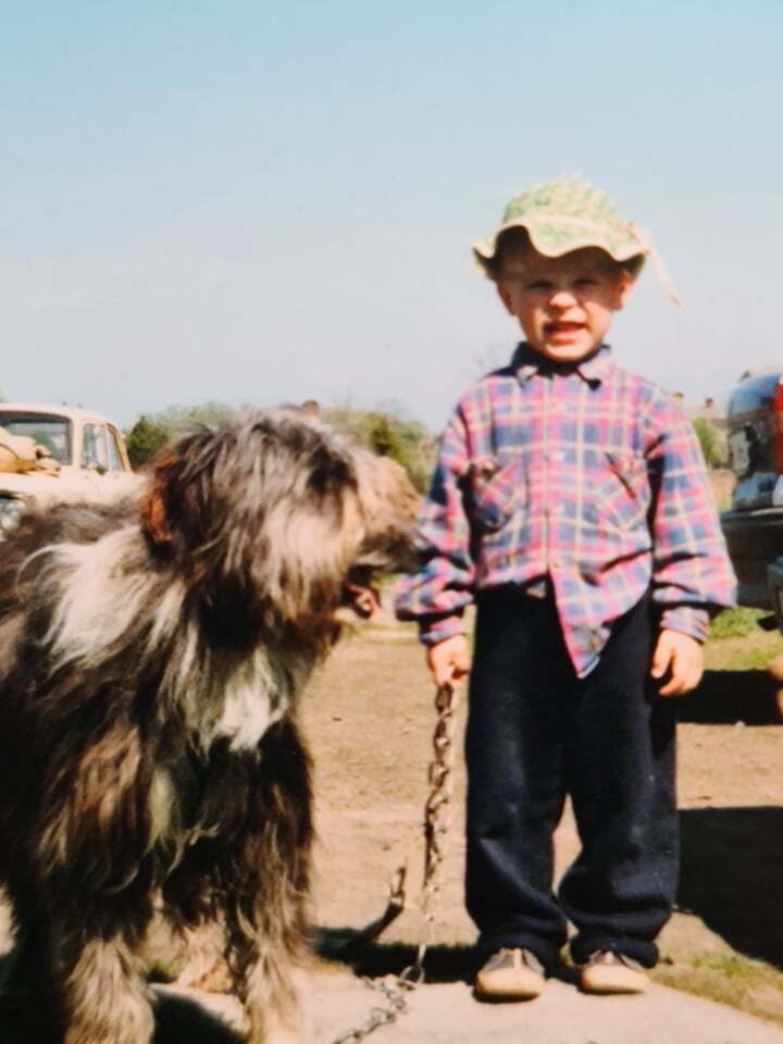 Young boy in a plaid shirt holding a chain attached to a large fluffy dog.