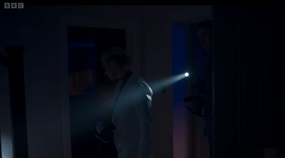 A person in a white suit uses a flashlight in a dark room.