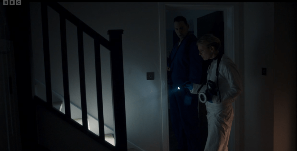 Screenshot from Silent Witness showing two investigators using a flashlight in a dimly lit hallway.