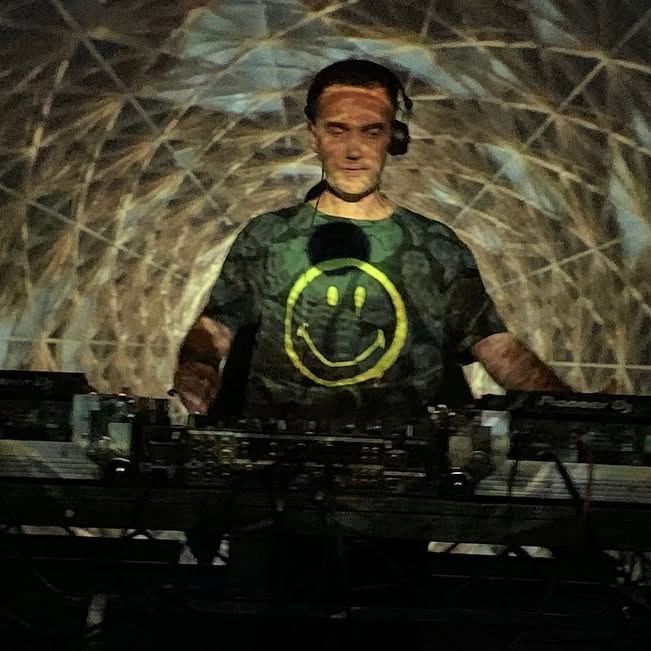 DJ at a mixer wearing a smiley face shirt.