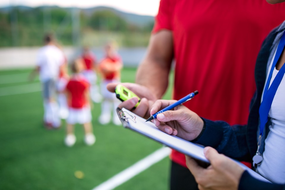 Coach taking notes on a clipboard while watching children play soccer.