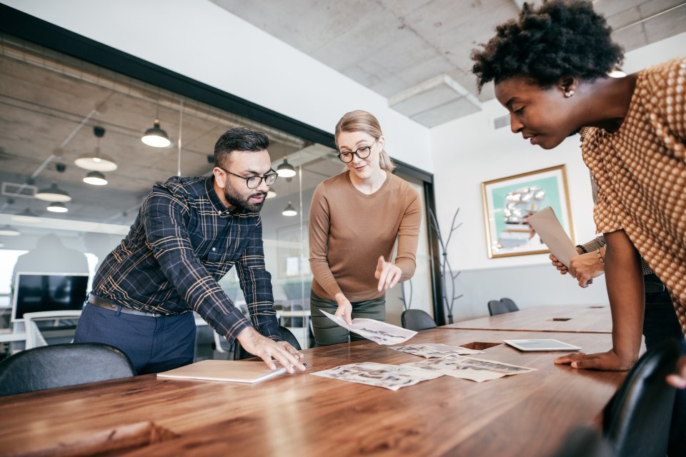 Three colleagues collaborate over documents at a conference table.