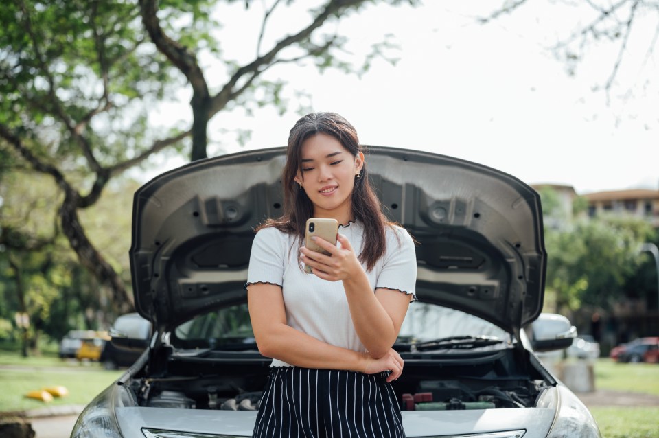 Woman using phone, car hood open.