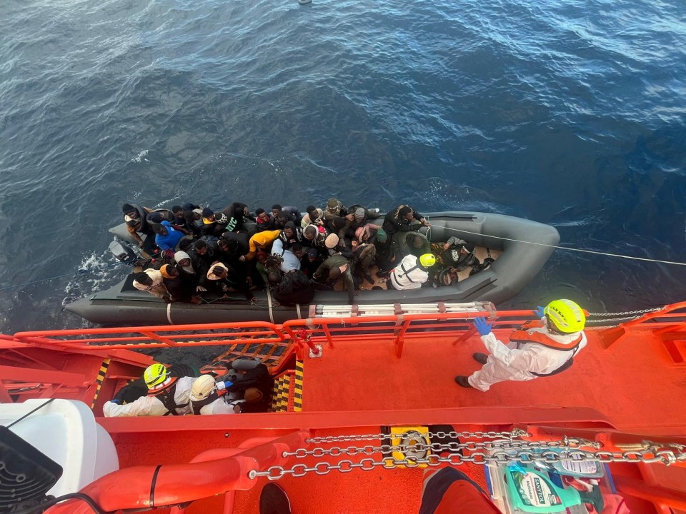 Spanish coast guards wearing white suits work on a rescue operation as they tow a rubber boat carrying migrants, including a newborn baby, off the island