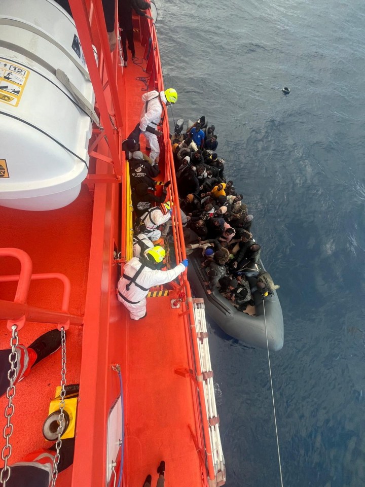 Spanish coast guards wearing white suits work on a rescue operation as they tow a rubber boat carrying migrants