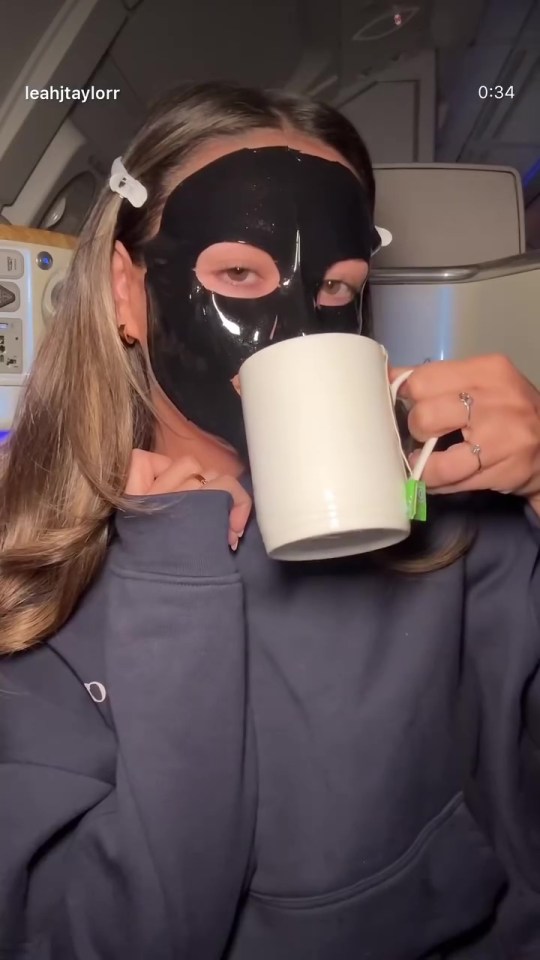 Woman wearing a face mask drinks tea on a plane.