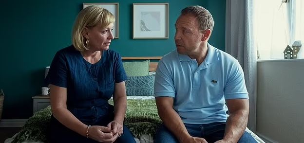 Couple sitting on a bed, talking.