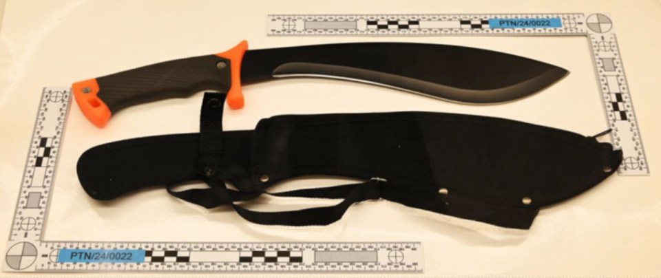 A machete and its sheath on a white surface with a ruler for scale.