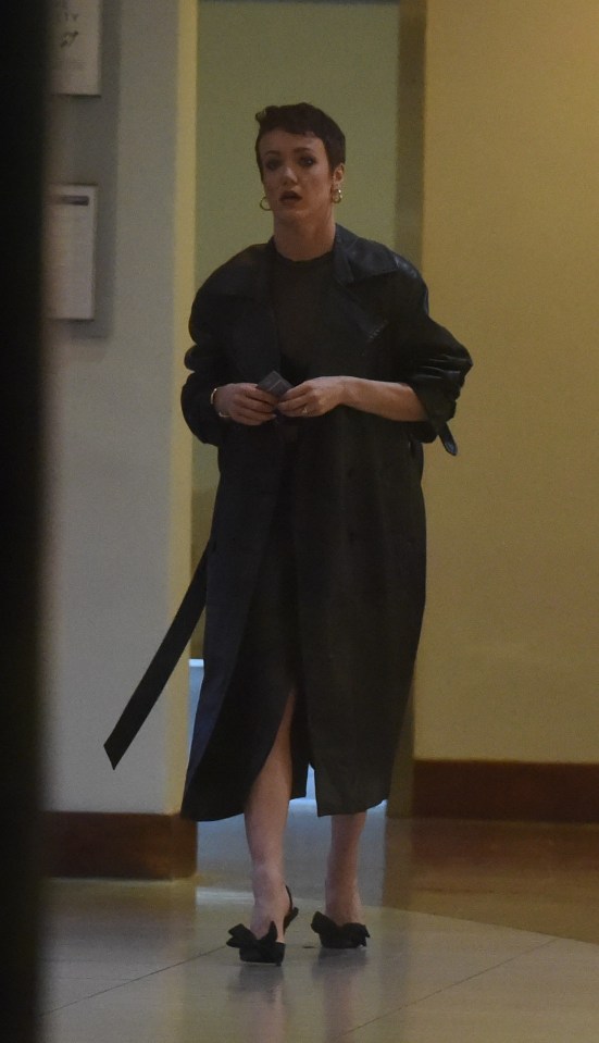 Woman in black coat and dress walking indoors.